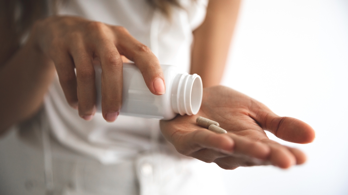 A woman taps a bottle of supplements into her palm, release a couple of capsules.