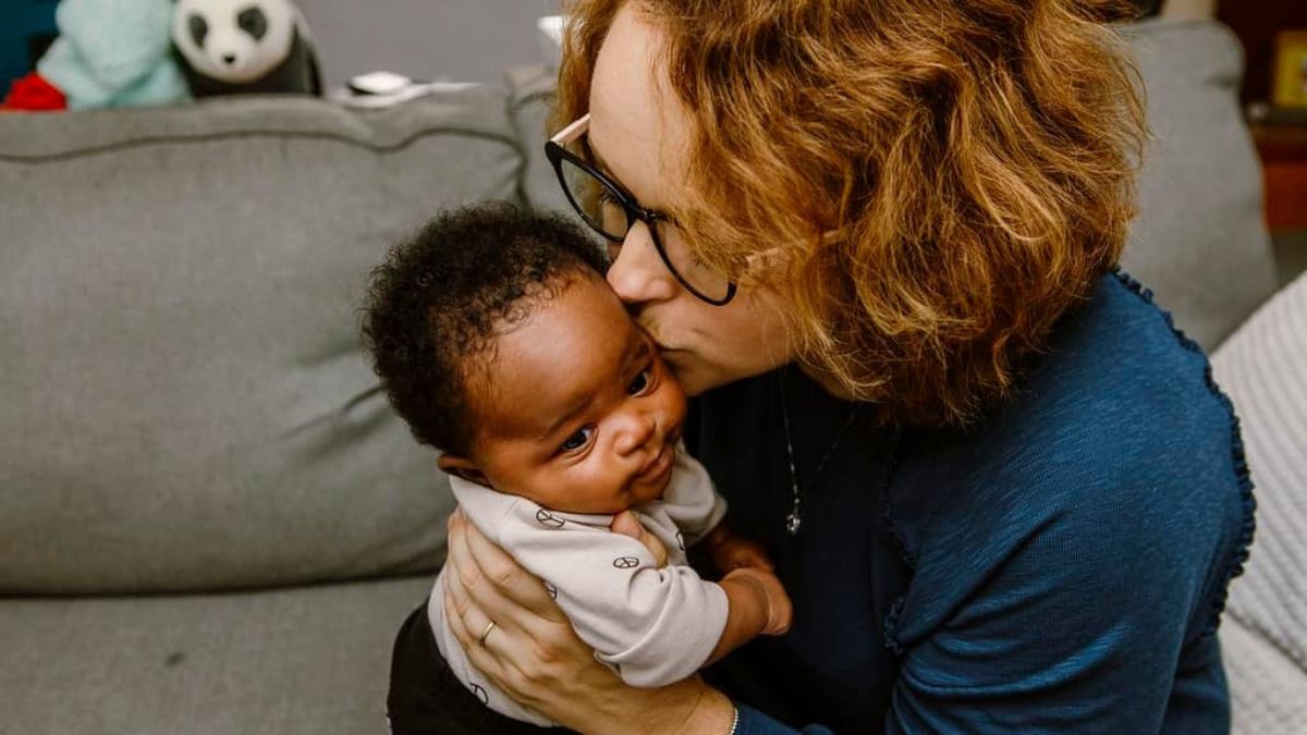 Liz holds her adopted baby daughter close, lovingly kissing her on the cheek.