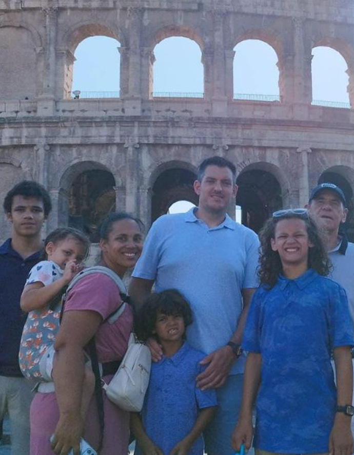 Angel Rinker, her husband, and their five children stand in front of the coliseum with two friends.