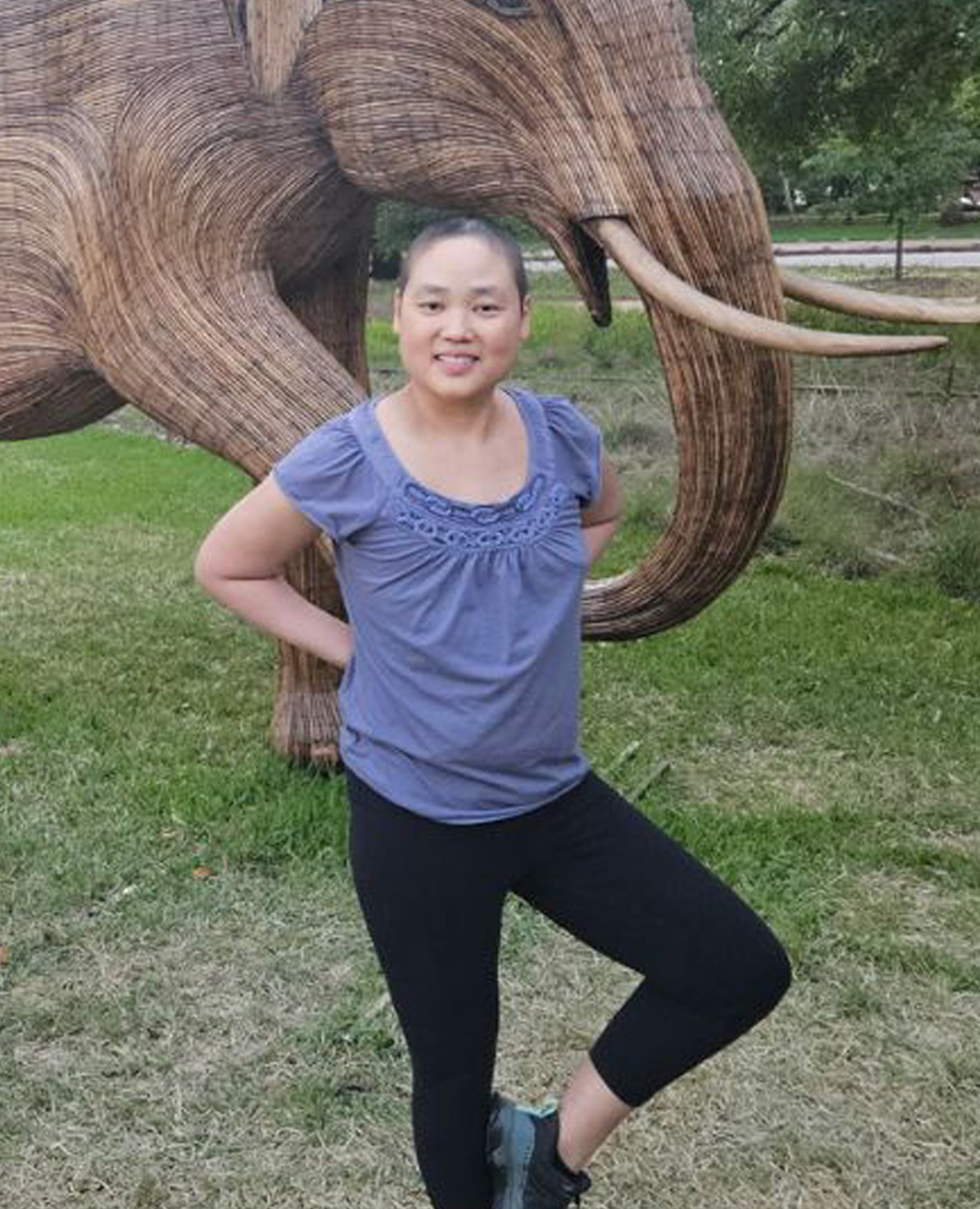 Christina Jue strikes a yoga pose in front of two realistic and beautiful elephant sculptures.