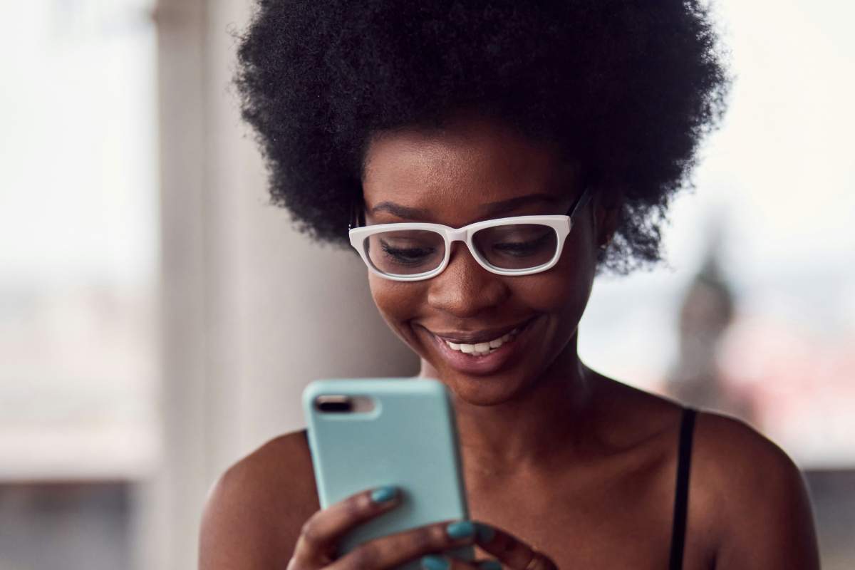 A Black woman smiling at her phone