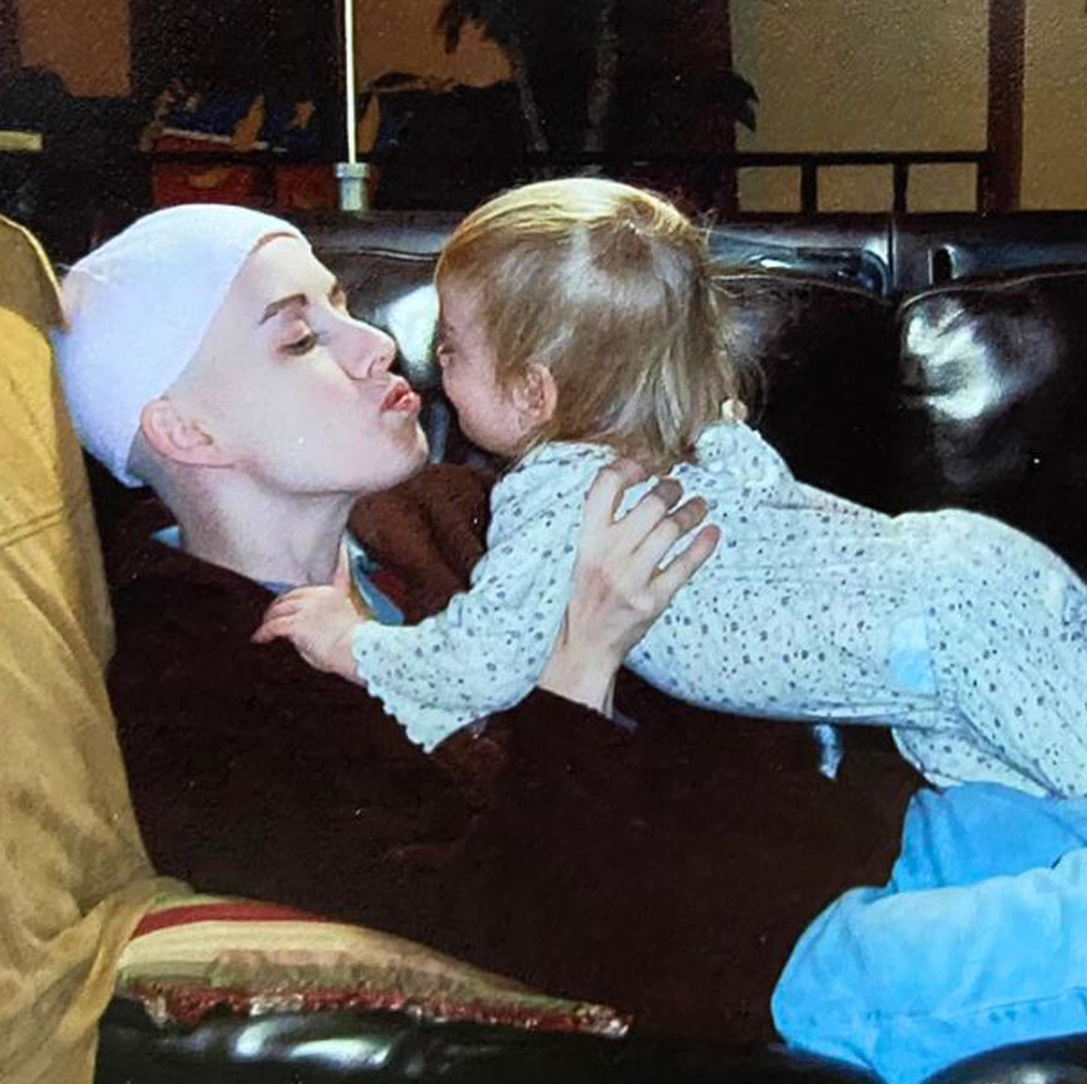 Klara Hartfiel kisses her baby daughter as she rests on the couch during her breast cancer treatment.