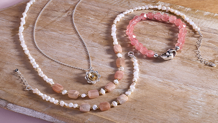 Two different bracelets and and two different necklaces laying out on a piece of wood.