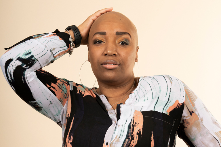 A Black woman with a shaved head looks straight at the camera