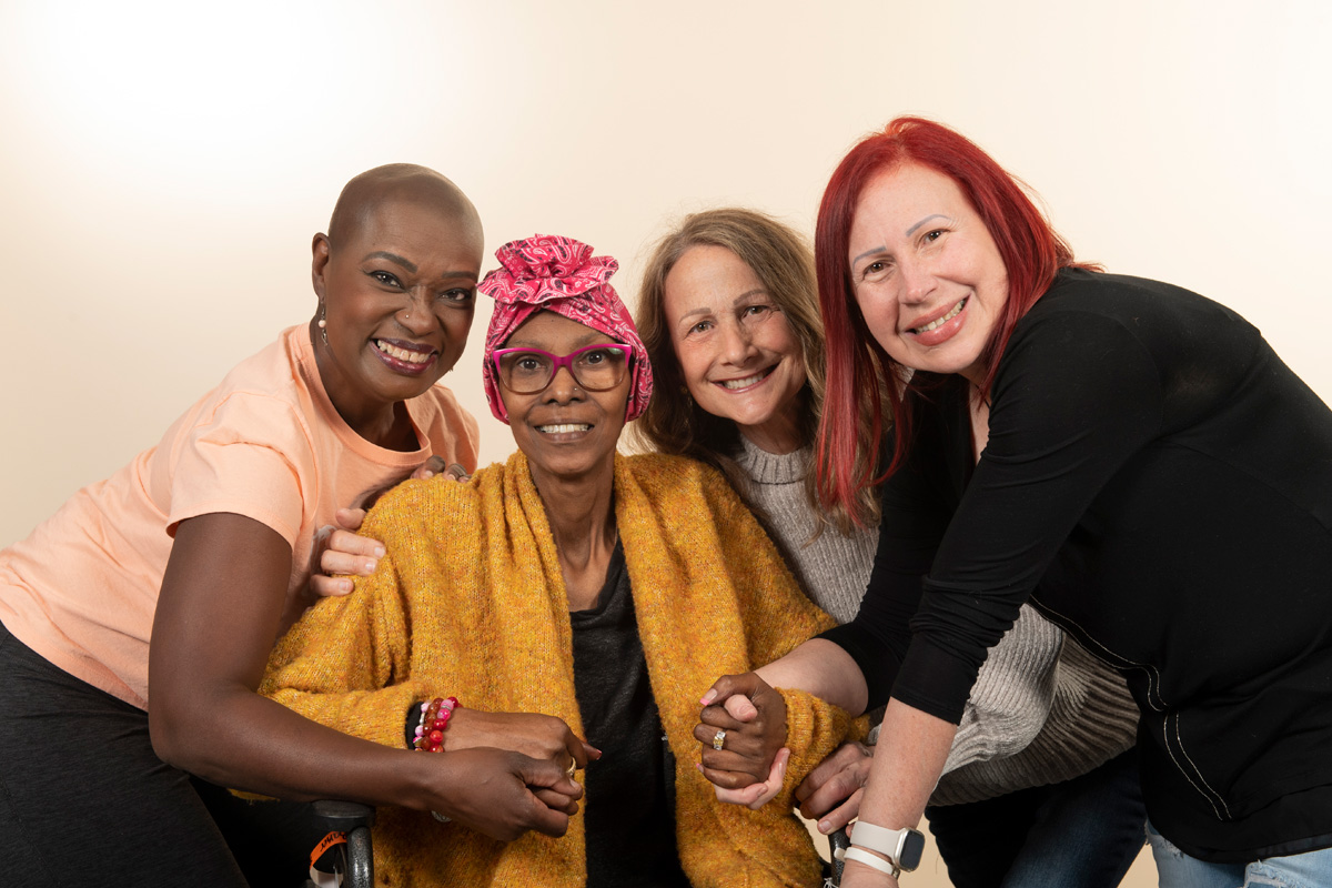 A diverse group of women holding hands and smiling with a Black woman in a wheelchair