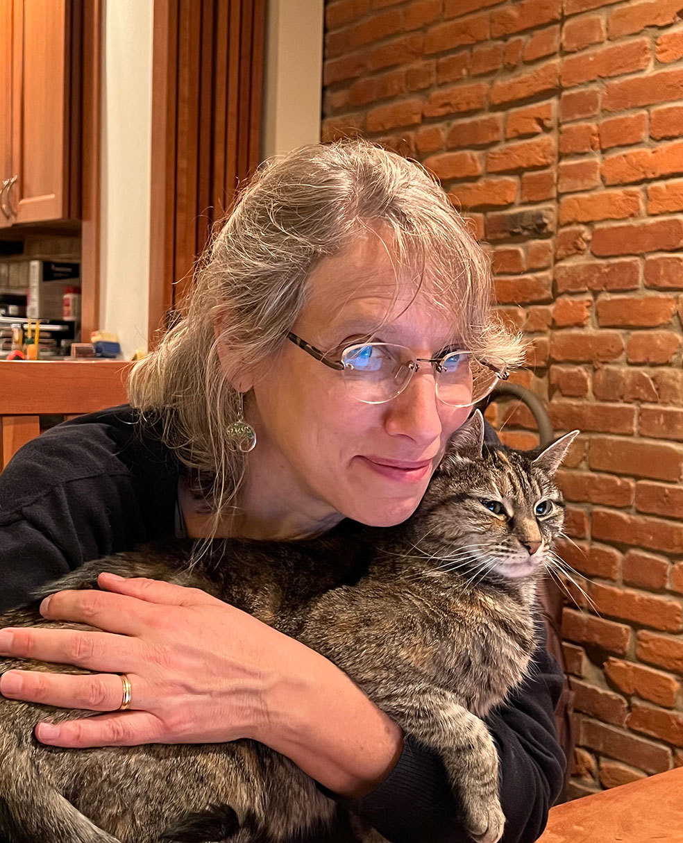 Kate, a white woman with glasses, hugs her cat