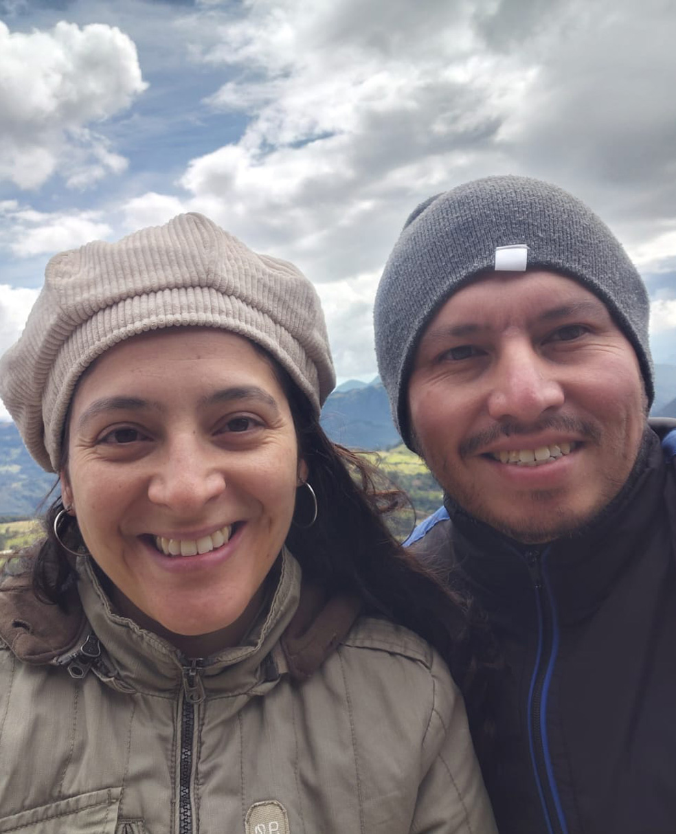 Gynna P. Quintero and her boyfriend Diego smile, mountain tops and big fluffy clouds behind them.