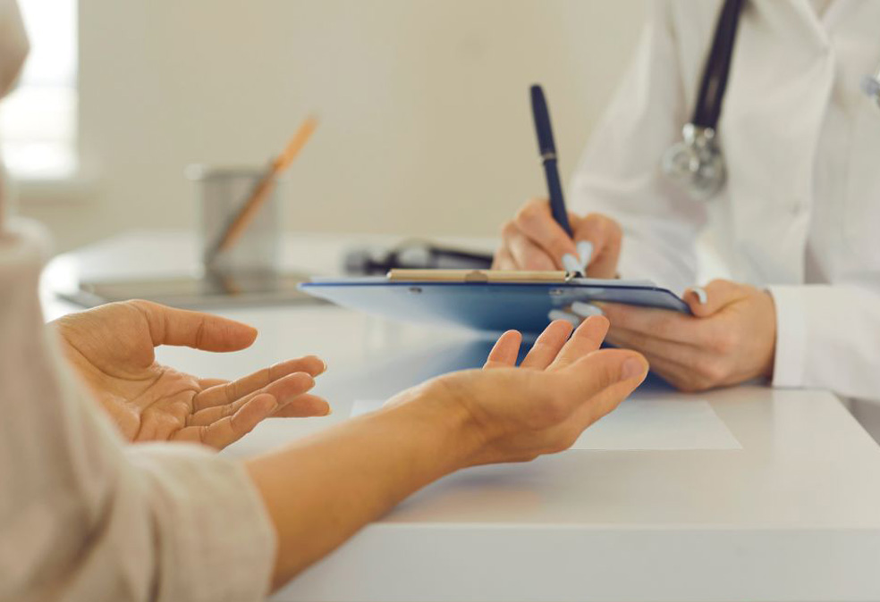 Hands are outstretched in front at a doctor's desk, asking for help.