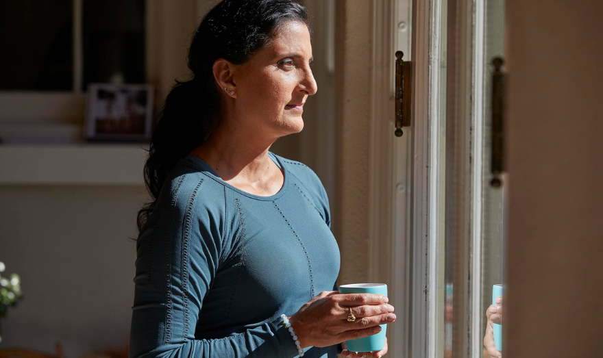 Woman looks out window with mug in her hand