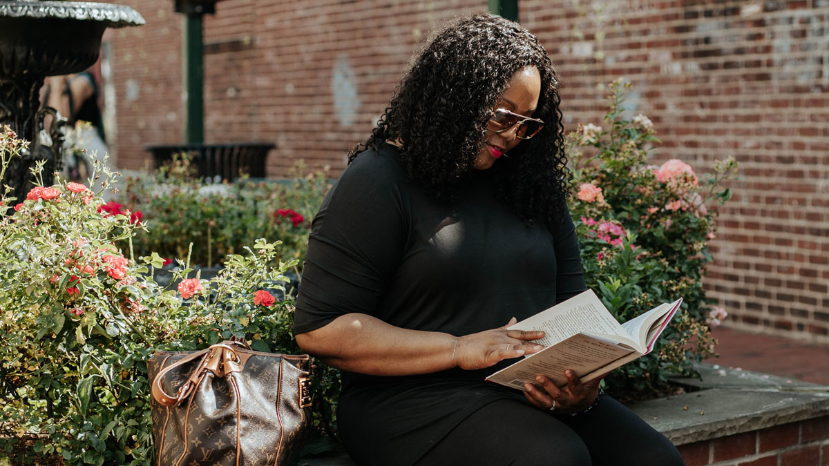 A Black woman with metastatic breast cancer sits outside reading a book