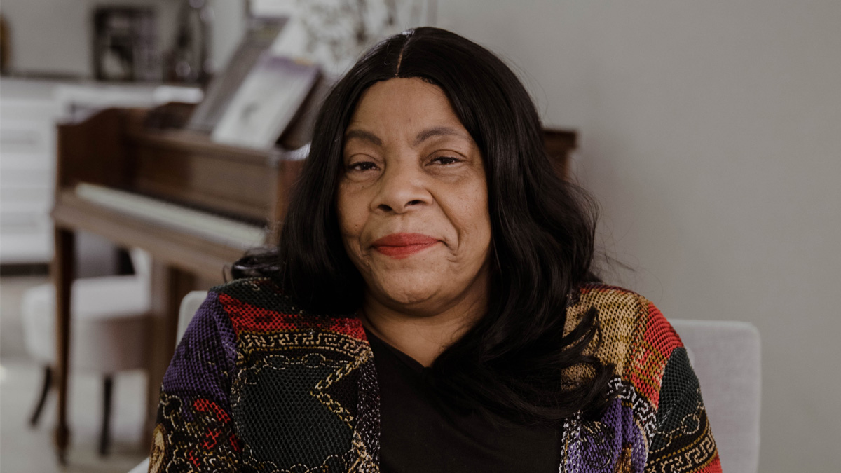 An older Black woman with a stoic look, sitting in a chair