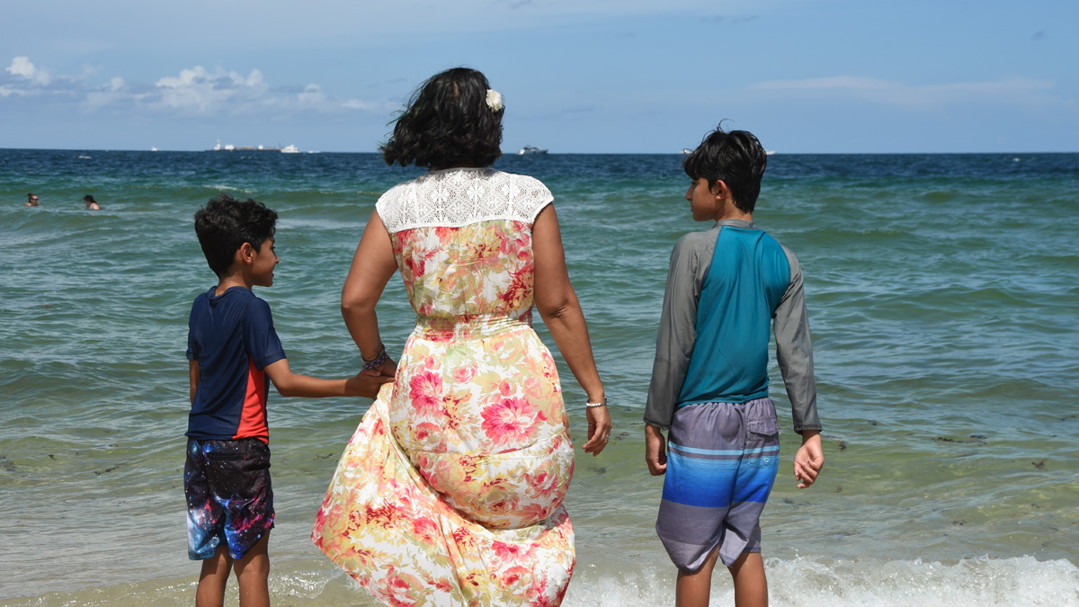 An Indian woman standing at the shoreline, chatting with her two young sons