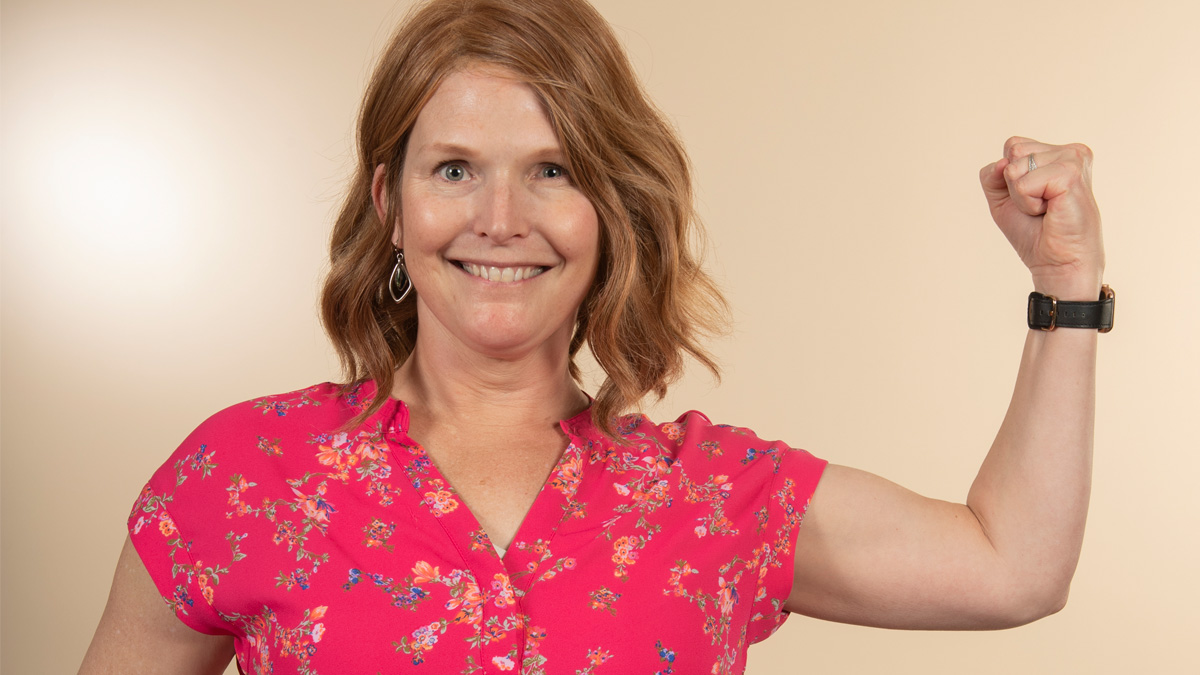 A white woman smiling flexing her arm muscle as a sign of strength