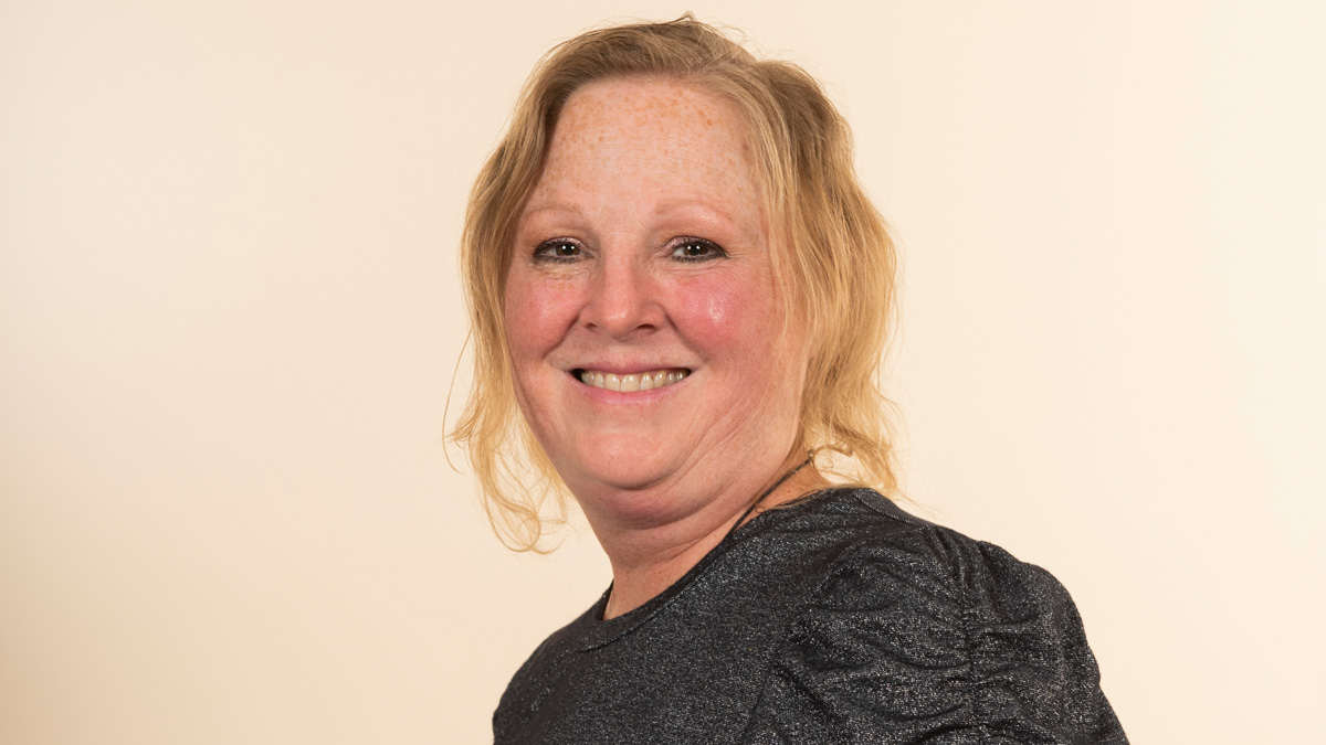 A white woman smiling in front of a beige background