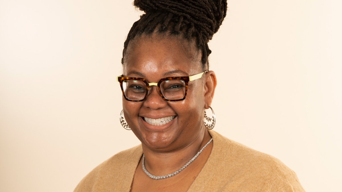 A Black woman with glasses and a bun on her head, smiling