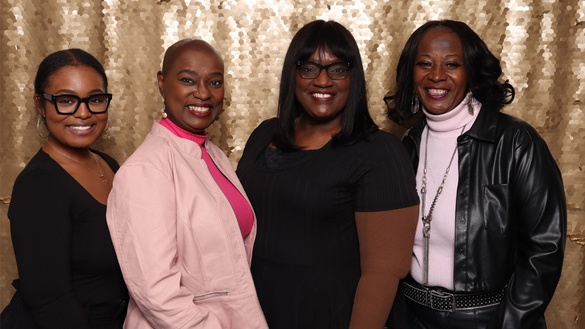 Four Black women smiling in front of a sparkly, gold backdrop