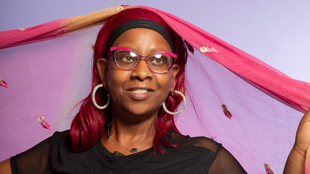 A Black woman smiling, holding a scarf draped over her head