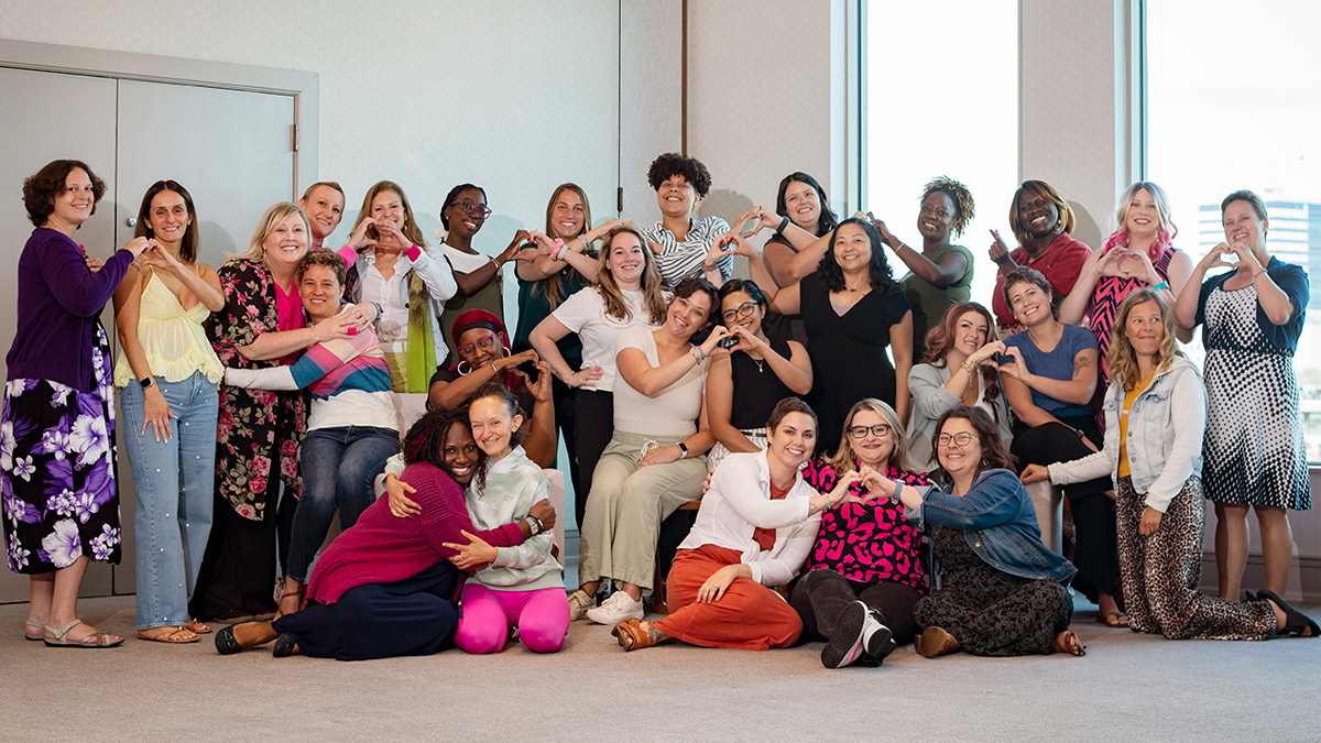 A diverse group of young women smiling and making hearts with their hands