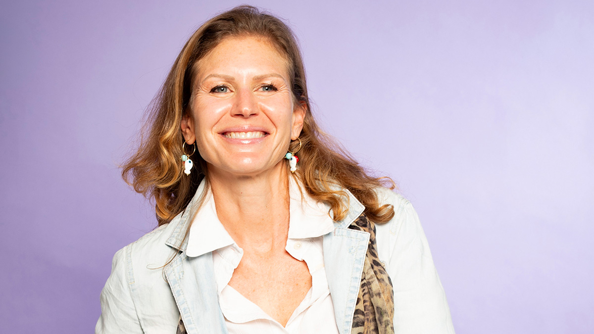 A white woman smiling in front of a purple backdrop