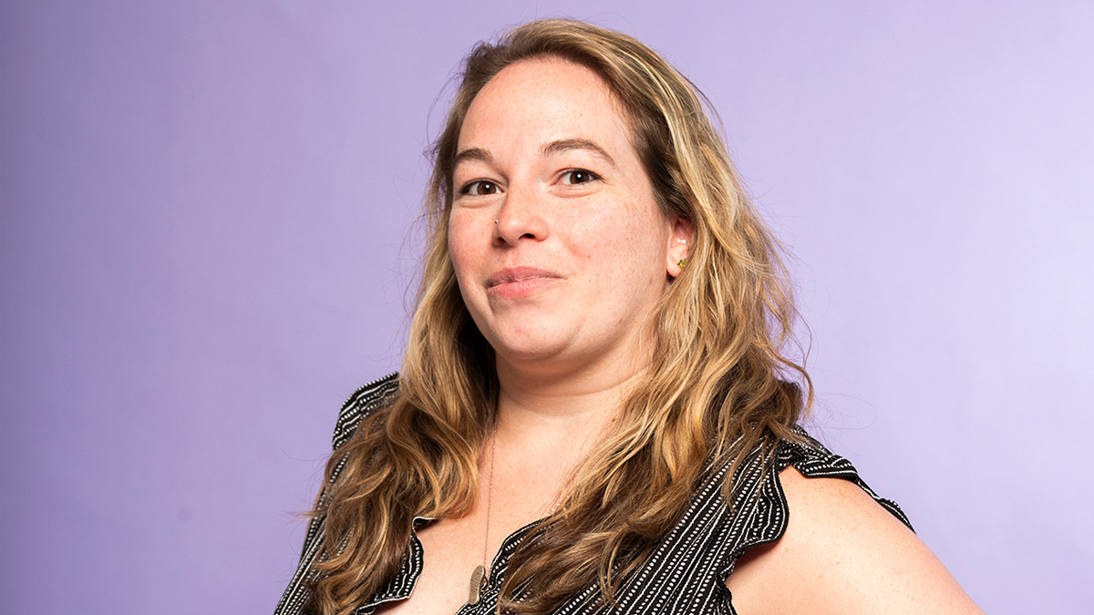 A white woman smiling in front of a purple backdrop