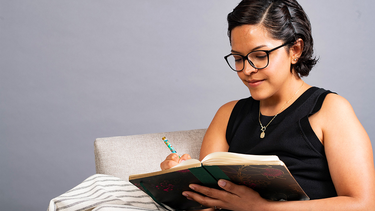 A Latina woman sitting in a chair, writing in a journal