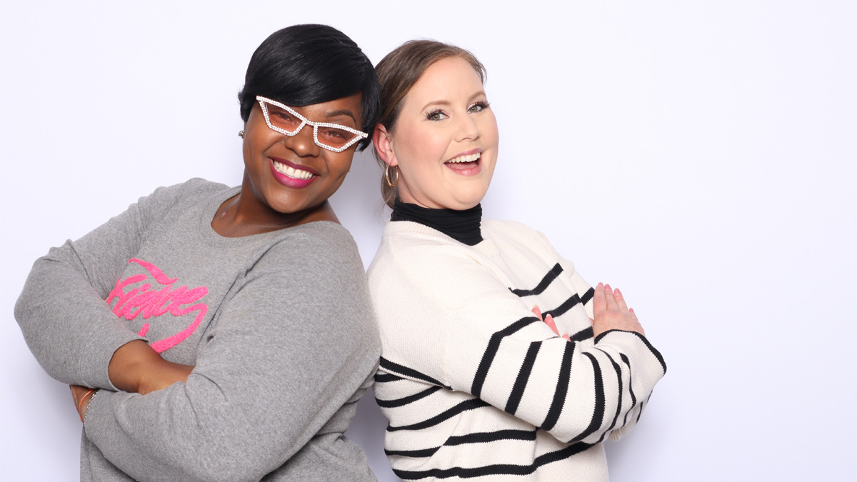 A Black woman and a white woman back-to-back, smiling.