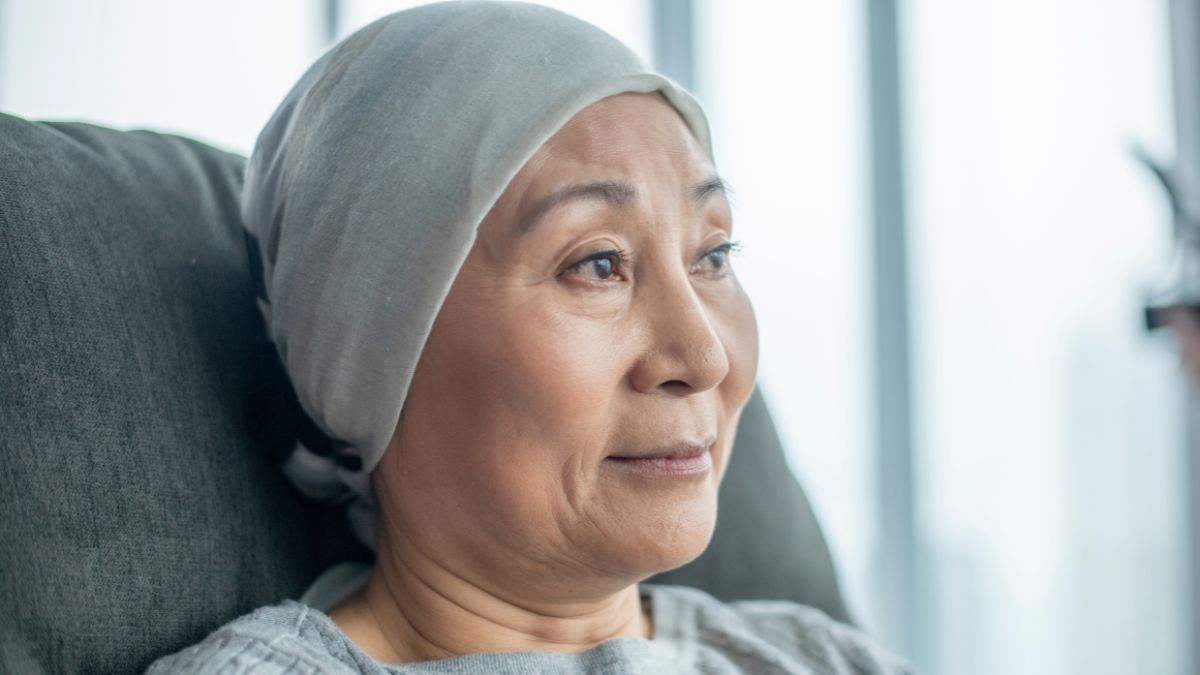 Older Asian woman with a head wrap sitting in a chair.
