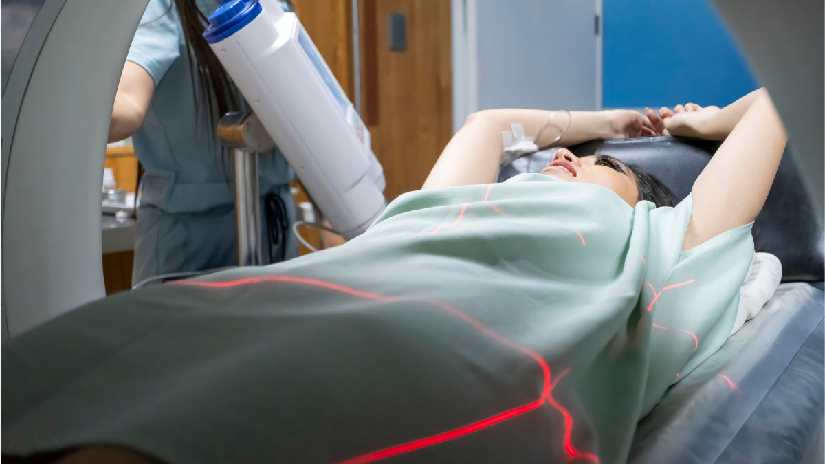 An Asian woman laying in a CT machine with her arms above her head