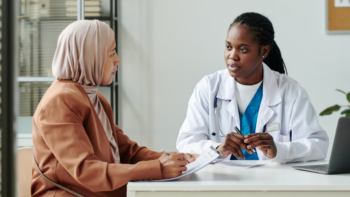 A woman wearing a hijab signing papers and talking to her Black female doctor