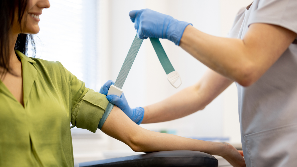 A white woman smiling in the doctor's office while the doctor is wrapping a torniquet around her arm for bloodwork