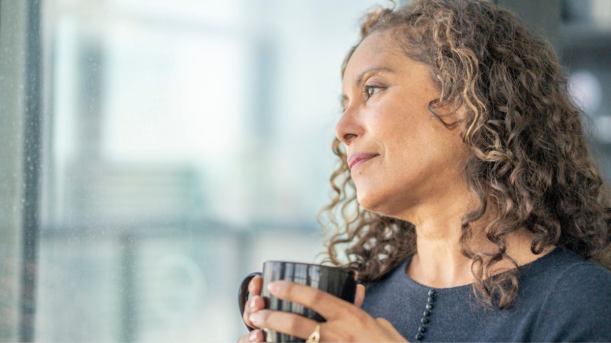 A Black woman staring out a window, holding a mug