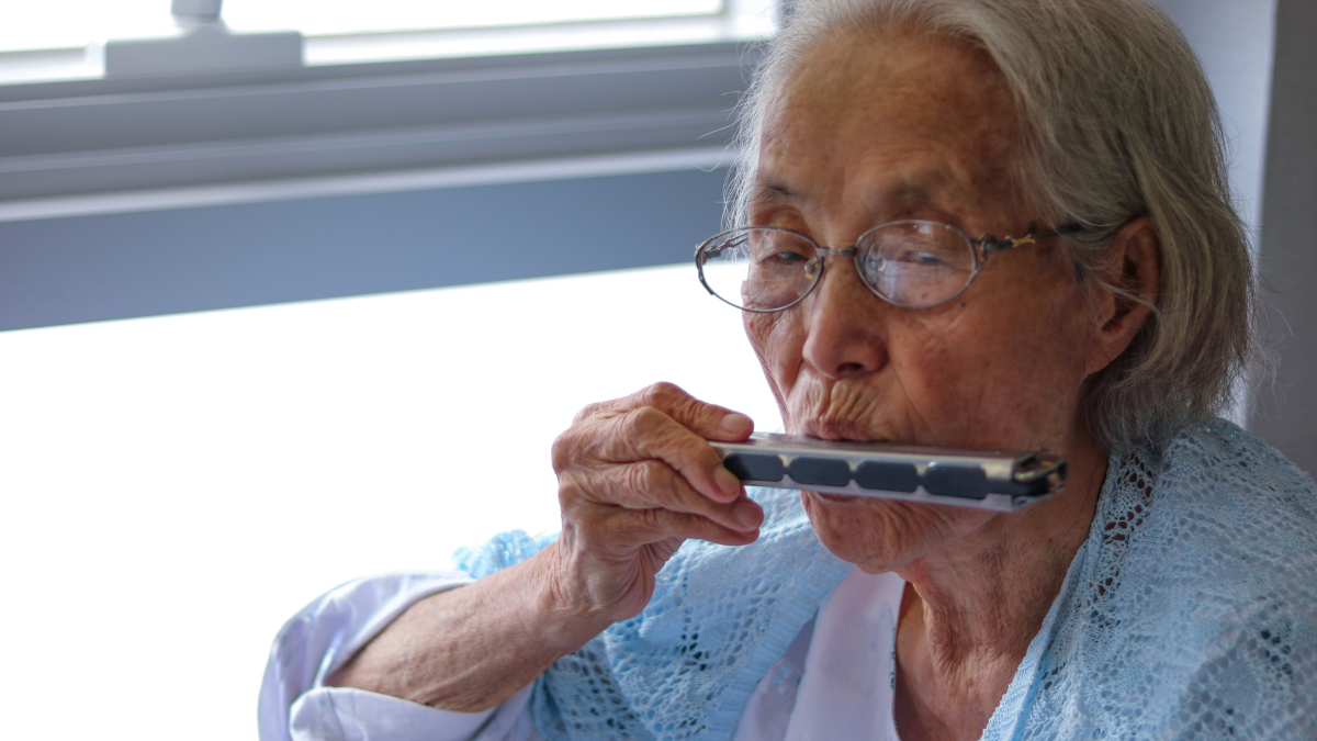 An elderly Asian woman using a harmonica