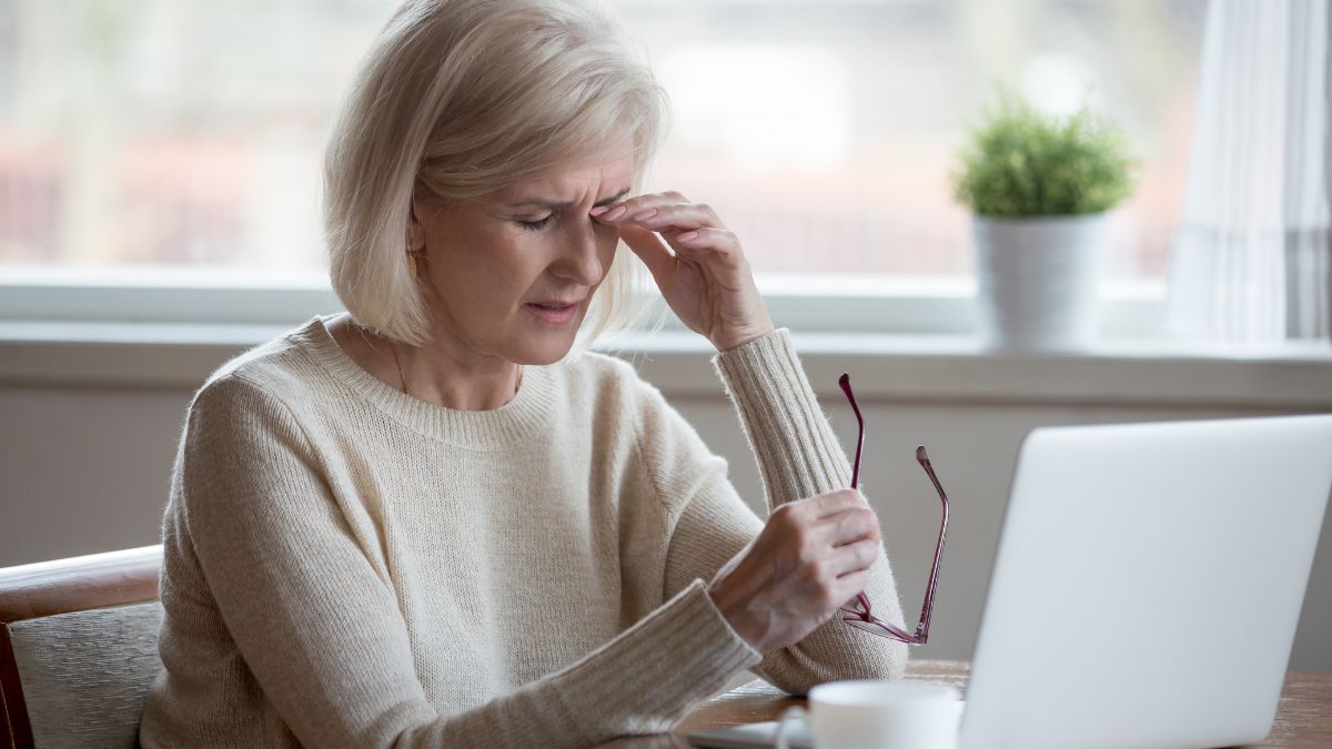 An older woman looking at her computer and rubbing her eyes in fatigue