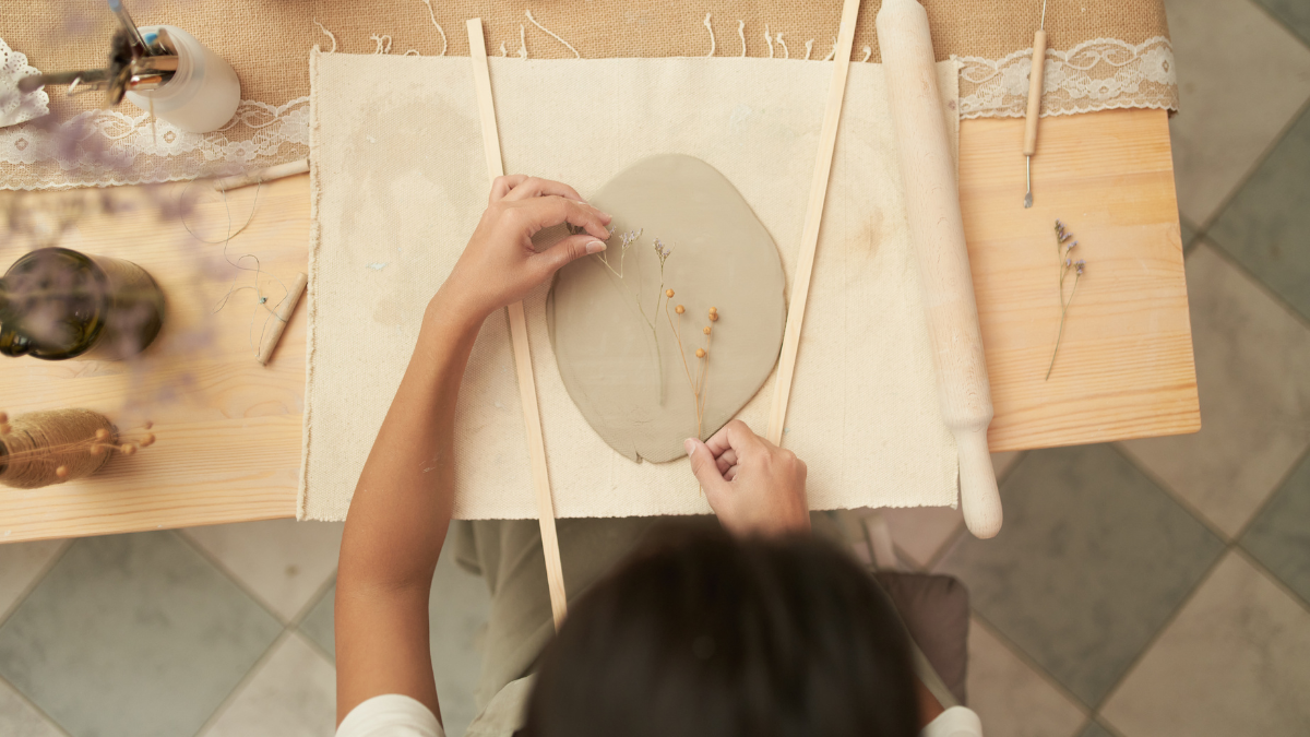 A racially ambiguous woman imprinting flowers onto a slab of clay