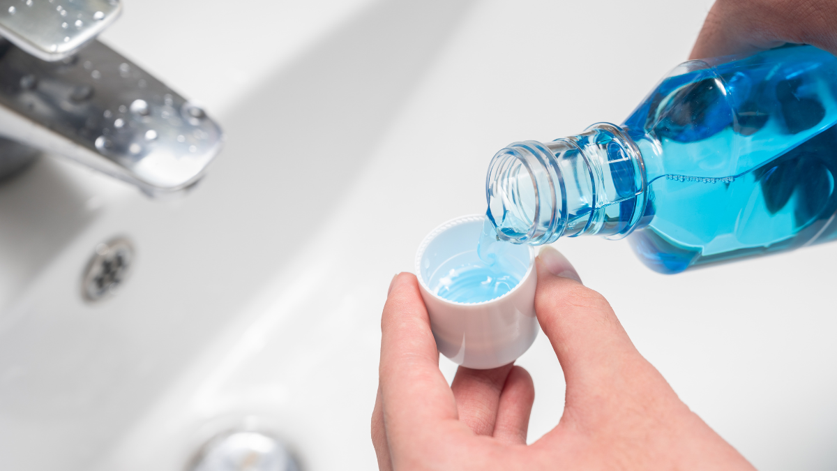A white woman's hands pouring mouthwash into a small cup over a sink