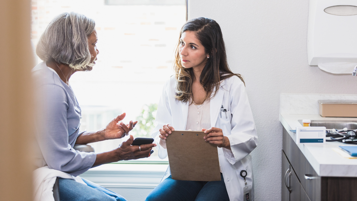 An Asian doctor intently listening to her patient, an older Black woman, talk to her.