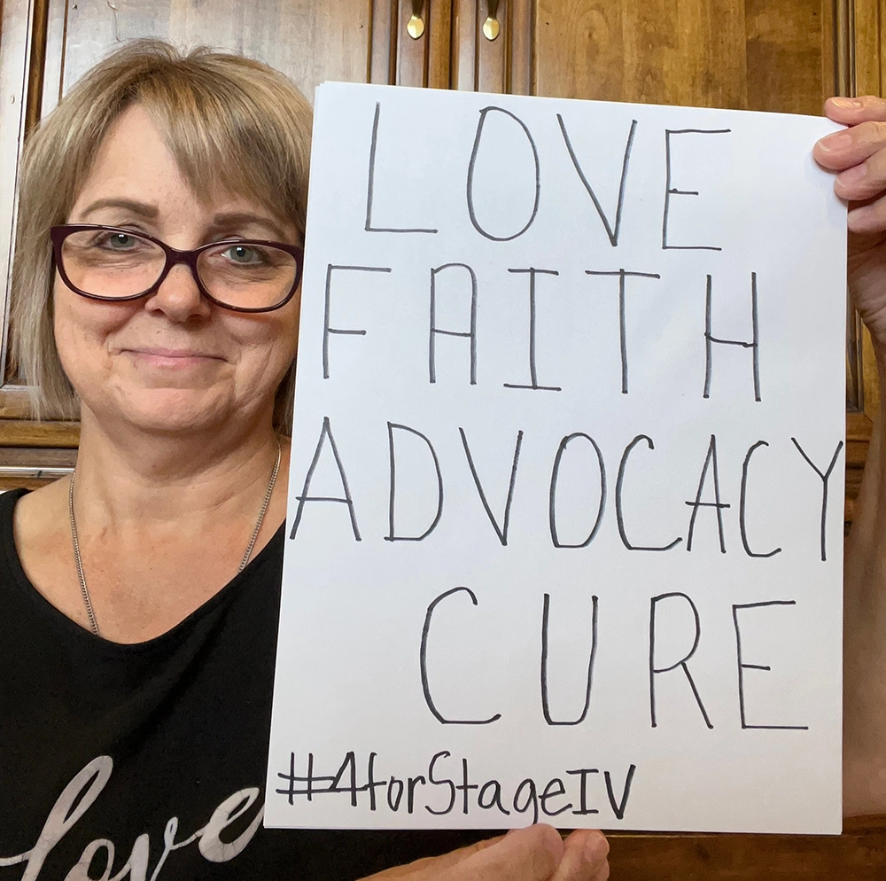 White woman holding sign with the words Love, Faith, Advocacy, and Cure written on it