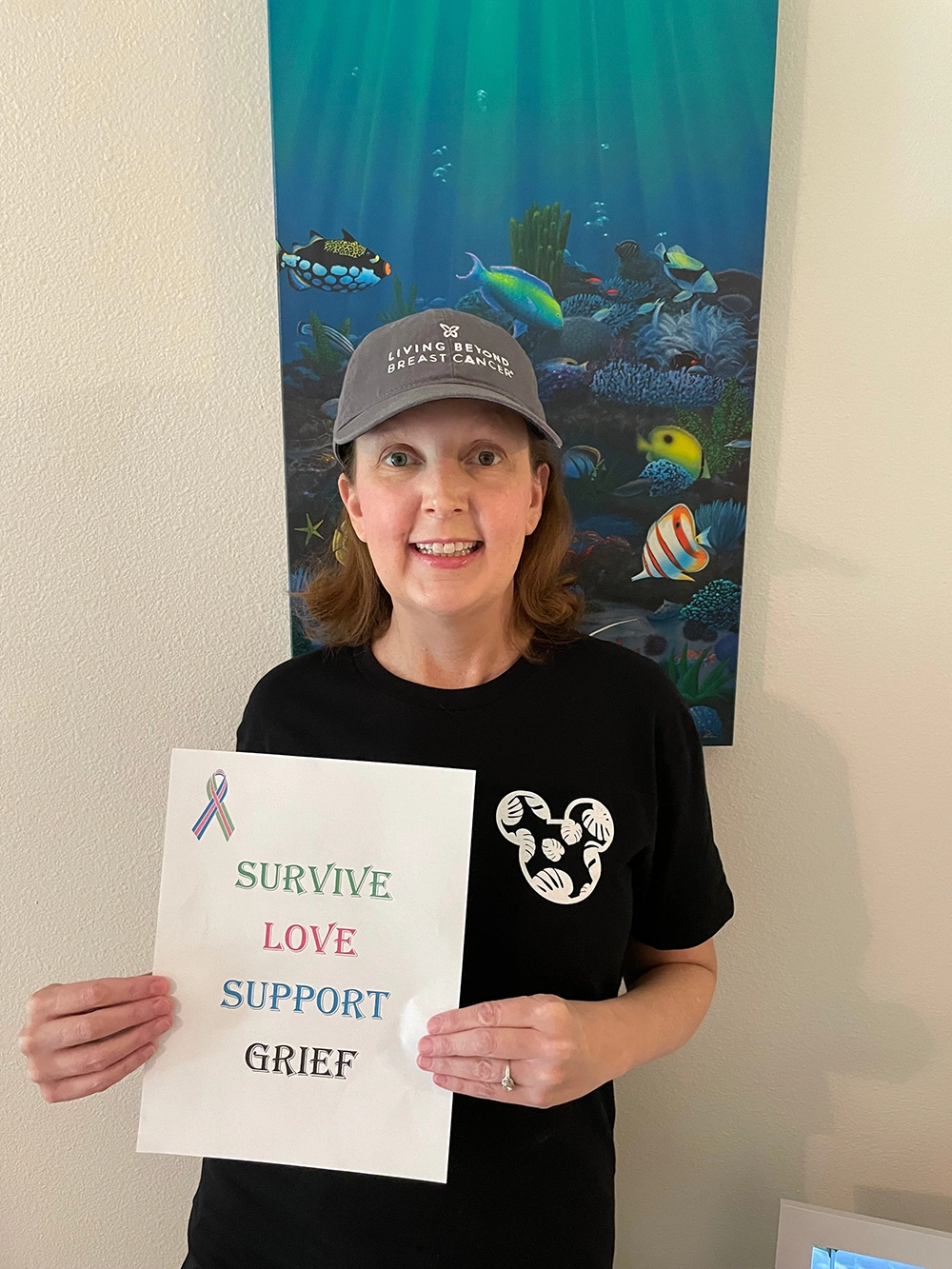 White woman with a small sign with the words Survive, Love, Support, and Grief printed on it in various colors