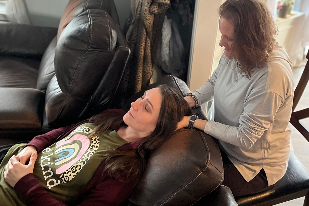 Amanda reclines in a comfortable chair while receiving a cranial massage from a woman seated behind her