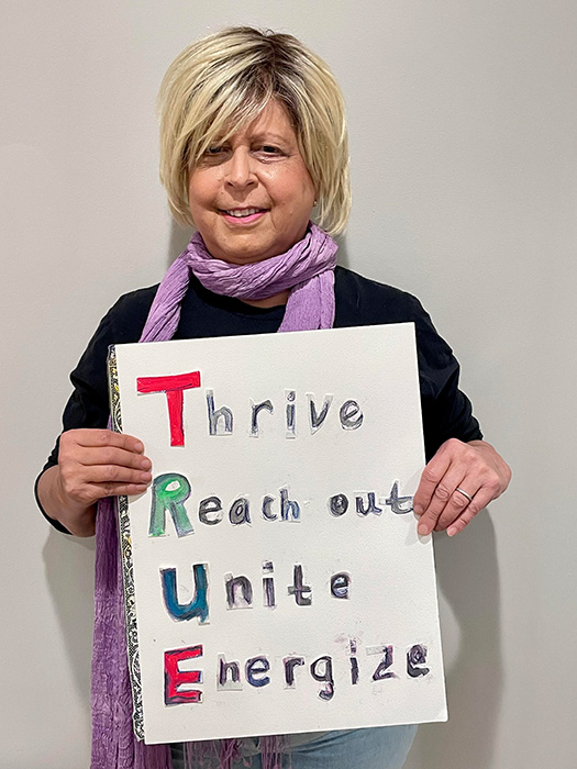 Chandler holding a sign that says Thrive, Reach out, Unity, Energize