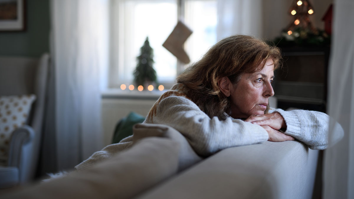 Woman leaning over back of couch, sadly looking out window