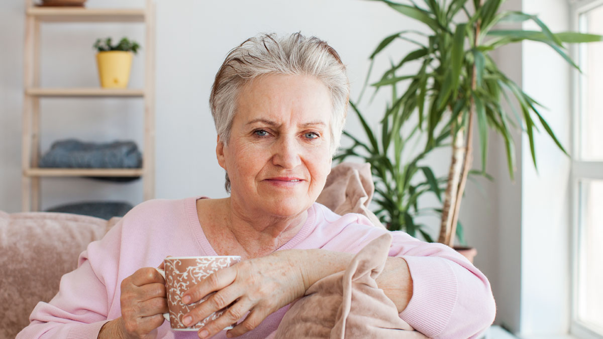 Mature woman looking at camera holding a cup of tea and smiling