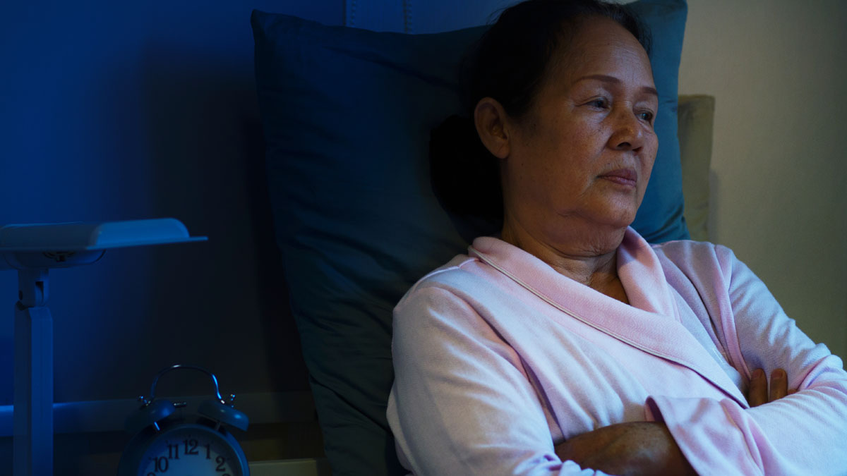 Woman sitting up in bed at night, deep in thought