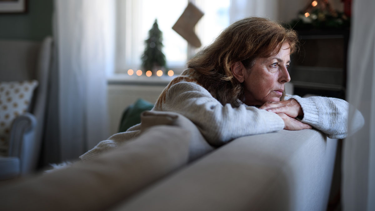 Woman leaning over back of couch, sadly looking out window