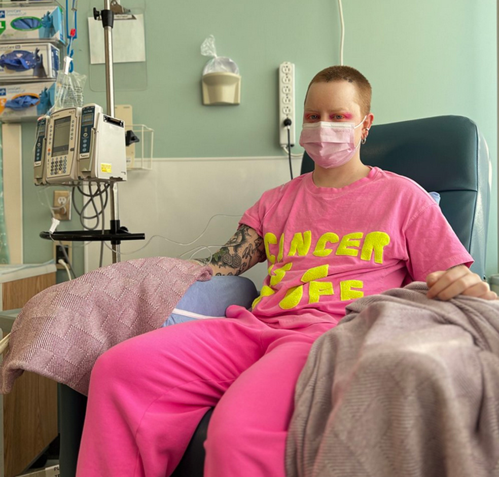 A masked Mike Hooves sits in a chemo chair, bright and defiant in pink