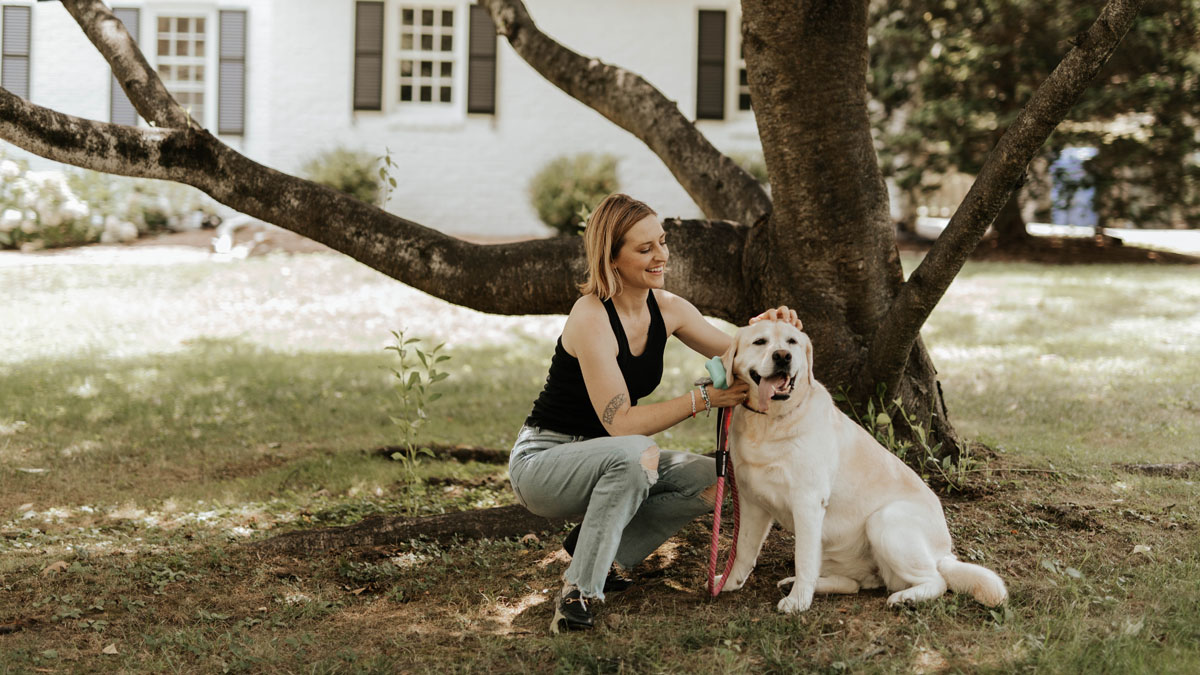 Woman petting dog under a tree