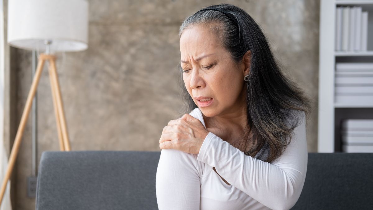 Older Asian woman grabs her shoulder in concern