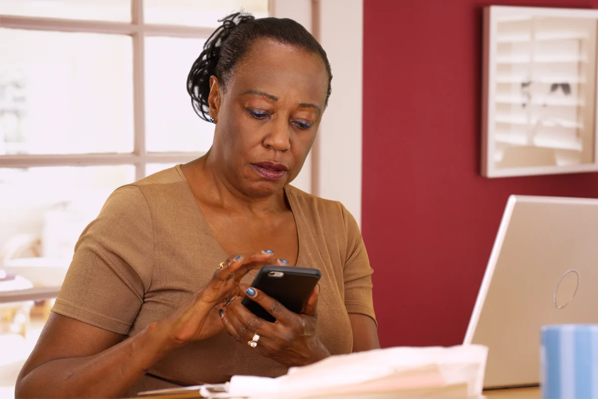 Black woman types on smartphone with a serious look on her face