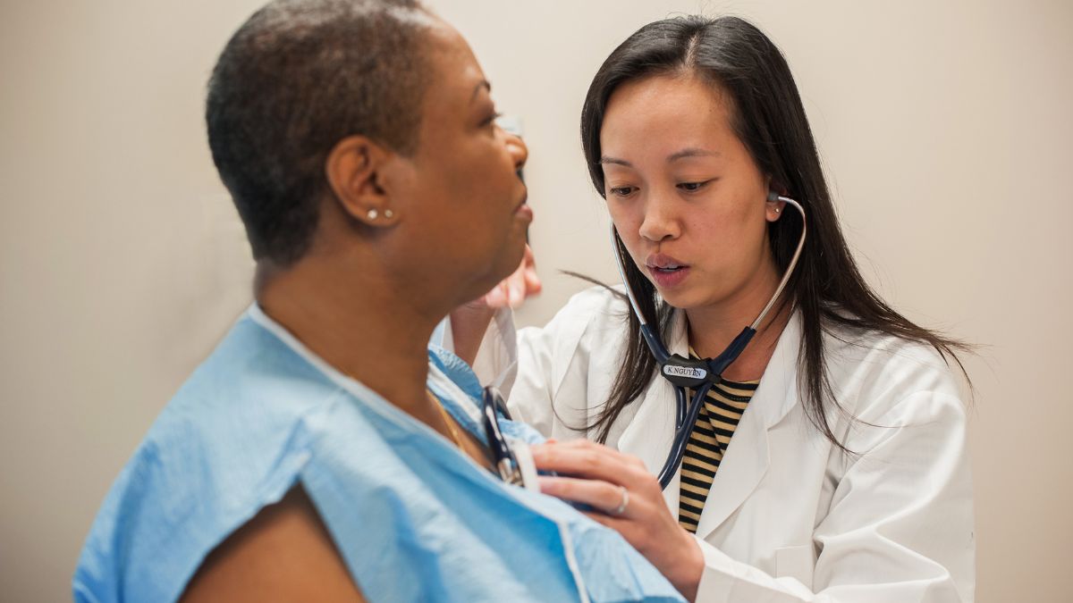 A Vietnamese doctor listens to a Black patient's heart with a stethoscope