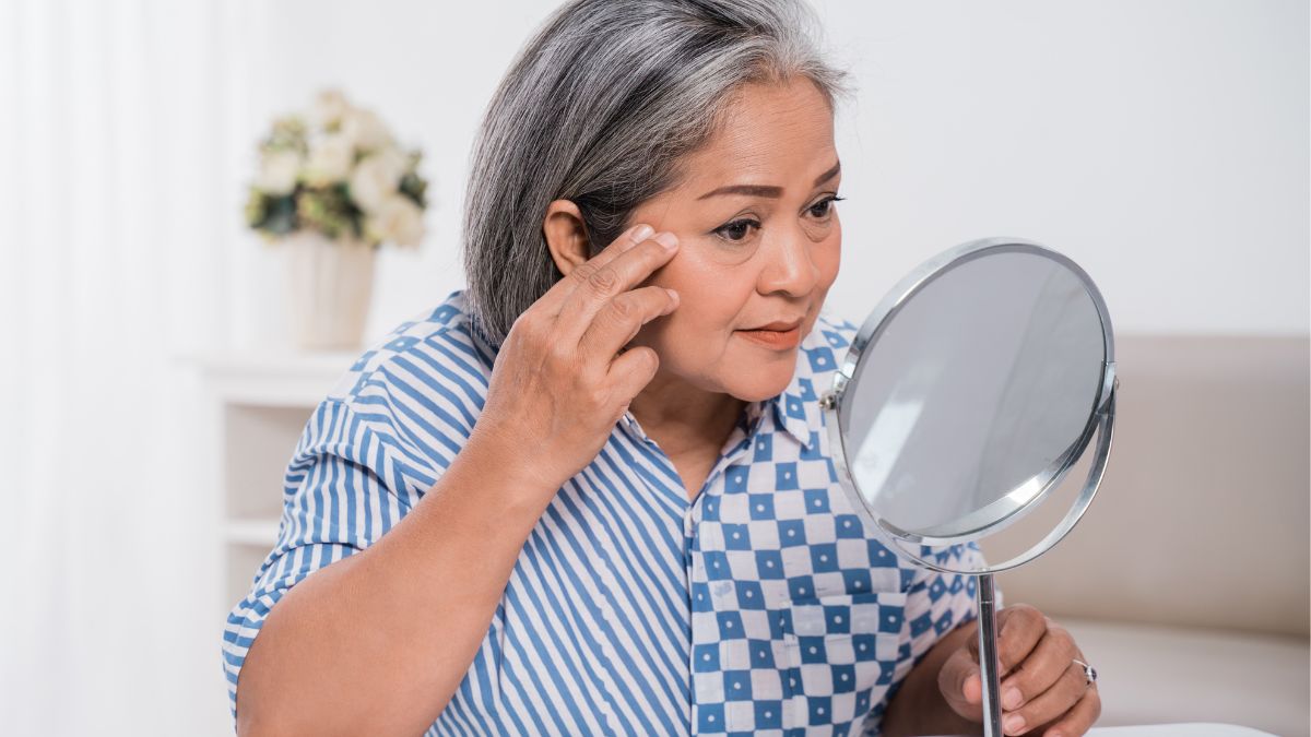 An older Asian woman looks into a mirror